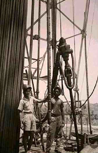 Archive photograph of two crew members on a drilling rig floor beside the kelly and hose